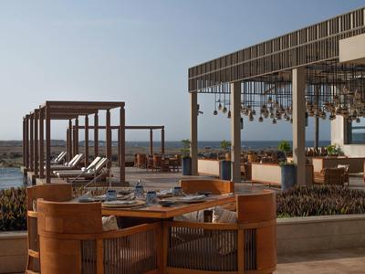 Terrasse extérieure moderne avec chaises en bois et lounge avec vue sur la mer au coucher du soleil.