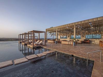 Espace piscine moderne avec chaises longues et pavillon ouvert au coucher du soleil.