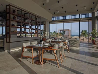Restaurante moderno con mobiliario de madera, grandes ventanales y vista al mar.