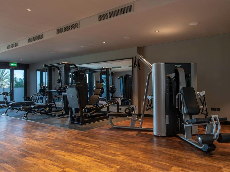Salle de sport moderne avec plusieurs appareils de musculation et sol en bois.