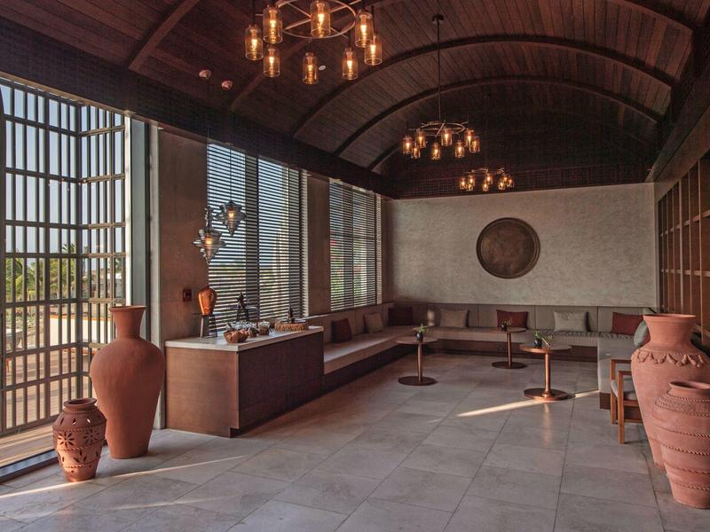 Espace lounge élégant avec grandes fenêtres, hauts plafonds et vases en terre cuite méditerranéens.