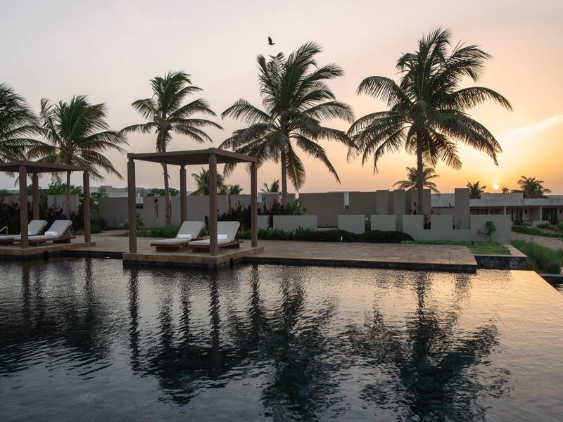 Coucher de soleil sur une piscine calme avec des palmiers et des transats.