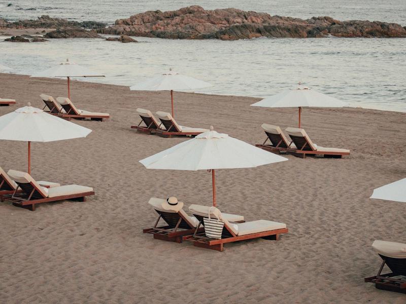 Chaises longues vides avec parasols blancs sur une plage calme avec des rochers en mer.