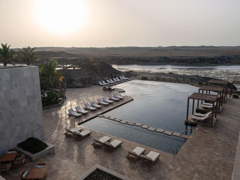 Piscine extérieure moderne avec chaises longues et vue sur un paysage fluvial paisible au coucher du soleil.