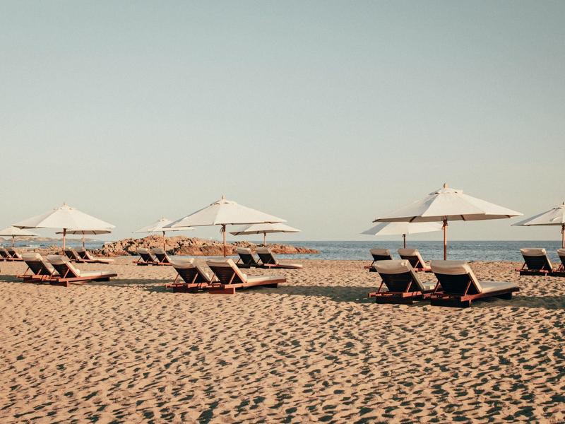 Alignement de chaises longues avec parasols blancs sur une plage de sable au bord de la mer.