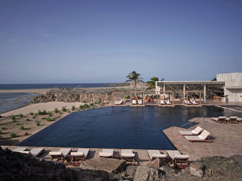 Grand bassin près de la mer avec chaises longues et palmiers dans un complexe hôtelier.
