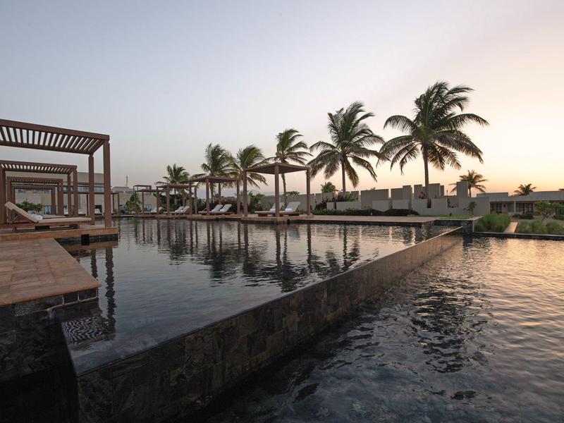 Piscine moderne avec palmiers et pavillons au coucher du soleil dans une station.