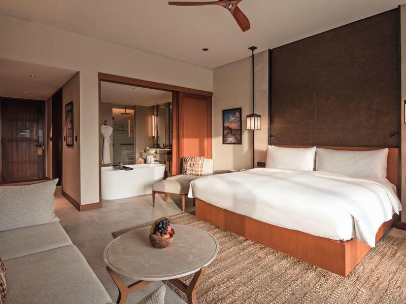 Chambre d'hôtel lumineuse avec lit double, canapé et salle de bain moderne avec baignoire îlot.