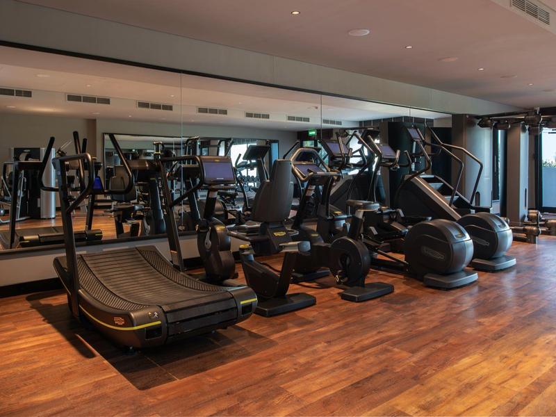 Salle de sport moderne avec tapis de course et autres équipements, sol en bois.