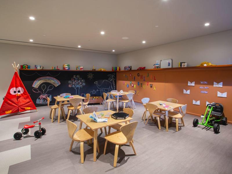 Salle de jeux et d'activités manuelles pour enfants avec petites tables en bois, tente colorée et jouets.