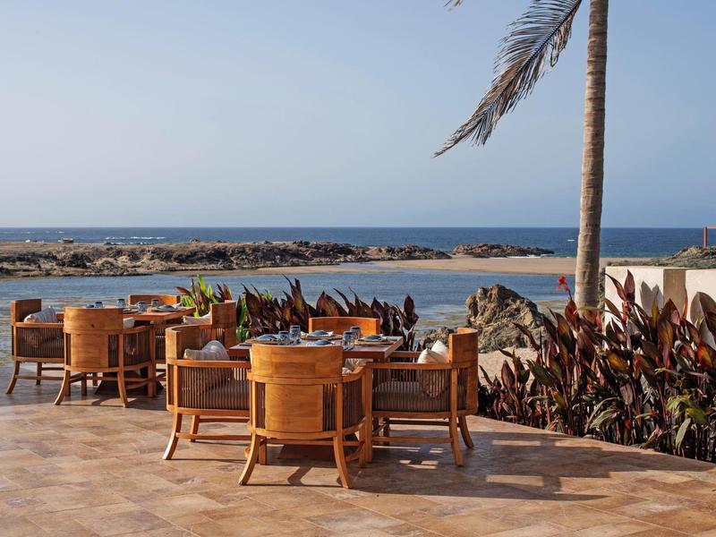 Terrasse avec tables et chaises en bois au bord de la mer sous un ciel clair
