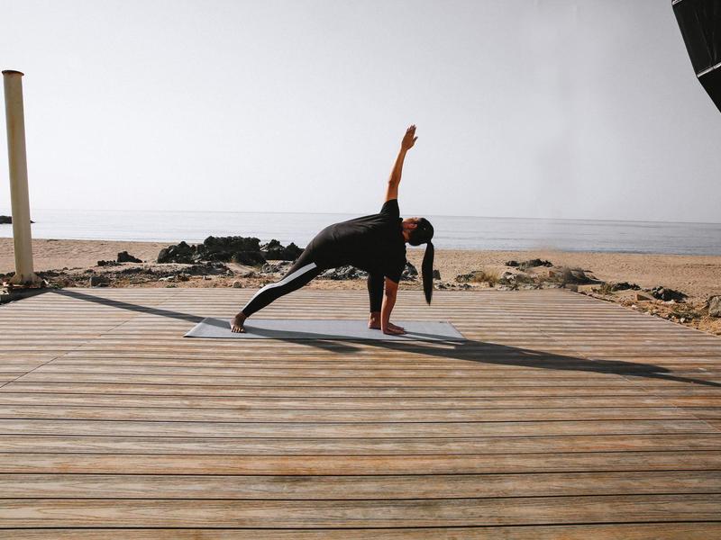 Person fait du yoga sur une planche en bois avec la mer en arrière-plan.