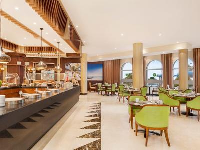 Lichte hotel eetzaal met buffet en groene stoelen bij tafels.