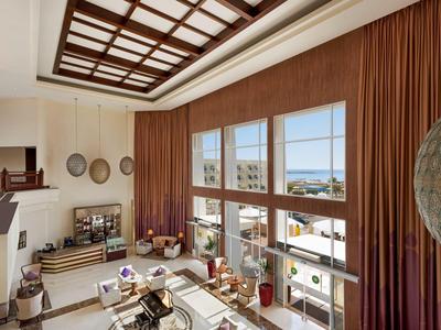 Ruime hotel lounge met hoge ramen en uitzicht op zee.