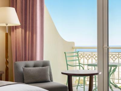 Lichte hotelkamer met balkon, stoel, tafel, fauteuil en uitzicht op de blauwe lucht.