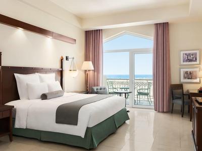 Lichte hotelkamer met groot bed, balkon en uitzicht op zee.