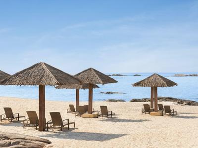 Leeg zandstrand met strooien parasols en ligstoelen bij rustige zee.