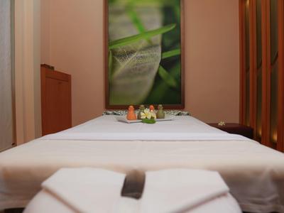 Een rustige massageruimte met een wit bed en kalmerende plantenmuurdecoratie.