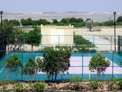 Sportplatz mit Tennis- oder Basketballfeld, umgeben von Grünflächen und Büschen.