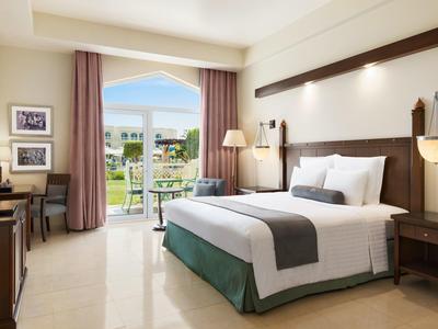 Lichte hotelkamer met tweepersoonsbed, bureau en uitzicht op terras met tuin