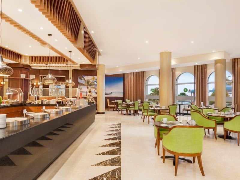 Lichte hotel eetzaal met buffet en groene stoelen bij tafels.