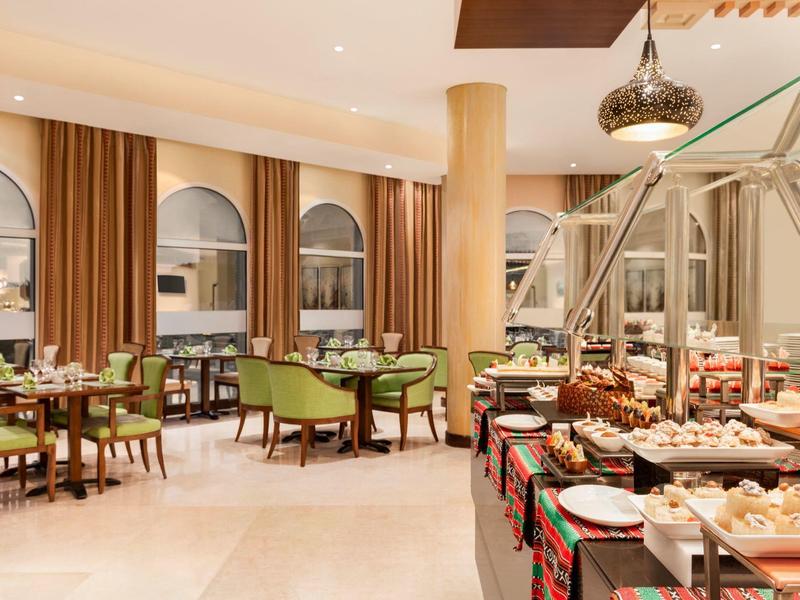 Elegante eetzaal met buffet en groene gestoffeerde stoelen in warme ambiance.