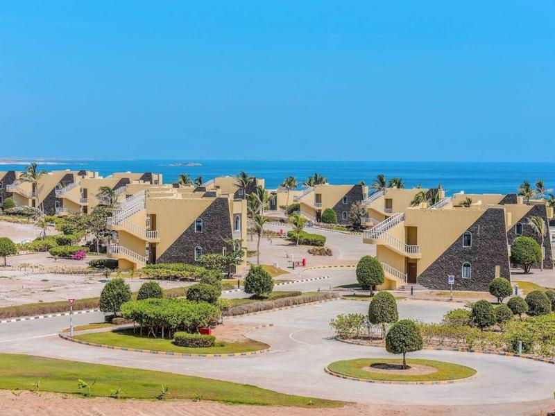 Rijen schuine gebouwen in een resort met uitzicht op zee onder een heldere blauwe lucht.