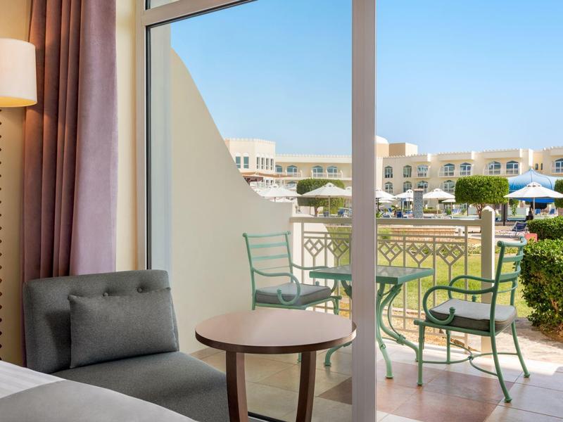 Hotelkamer met balkonzicht met tafel en stoelen, uitzicht op andere gebouwen bij heldere lucht.