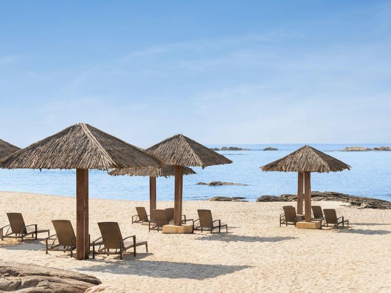 Leeg zandstrand met strooien parasols en ligstoelen bij rustige zee.