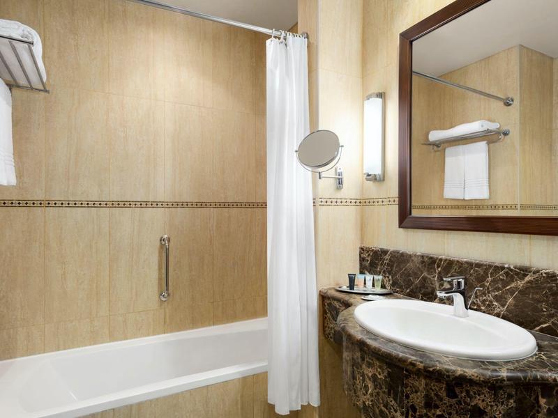 Schone badkamer met bad, witte douchegordijn, wastafel en grote spiegel.