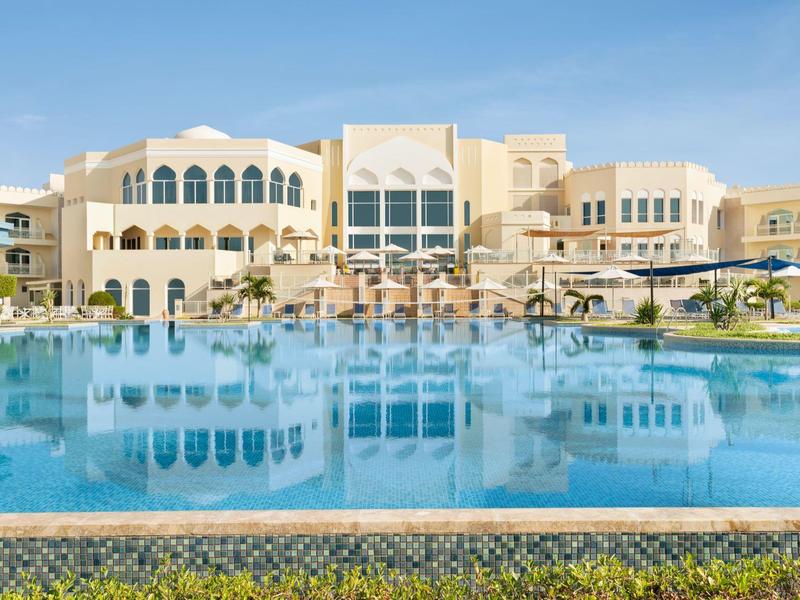 Groot meerlaagse hotelgebouw met een groot zwembad op de voorgrond.