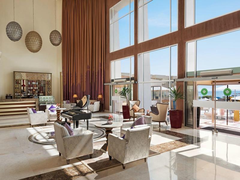 Lichte hotellounge met hoge ramen, zitgroepen en modern meubilair.