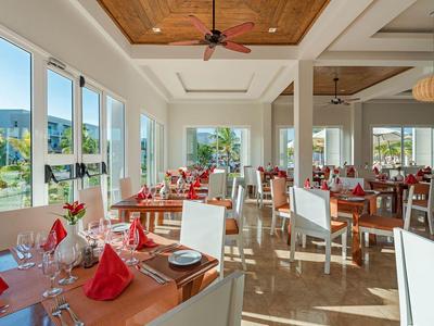 Helles Restaurant mit Holzboden, weißen Wänden, großen Fenstern und gedeckten Tischen mit roten Servietten.