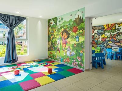 Heller Kinderspielraum mit buntem Teppich, Wandbild mit Tieren und angrenzendem Raum mit blauen Tischen.