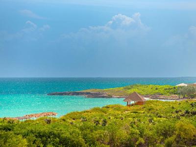 Grüne Küstenlandschaft mit türkisfarbenem Meer, Felsen und bewölktem Himmel im Hintergrund.