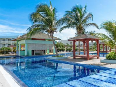 Moderner Außenpool mit klarem blauem Wasser, Palmen und Pavillon bei sonnigem Himmel.