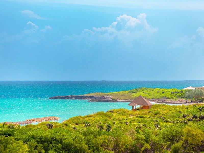 Küste mit grünem Busch, türkisfarbenem Meer und blauem Himmel mit leichter Bewölkung.