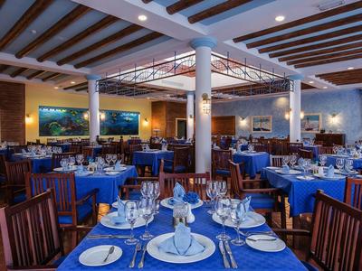 Großer Restaurantraum mit blauen Tischdecken, Holzmöbeln, weißen Säulen und Deckenstrahlern.