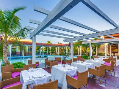 Außerbereichsrestaurant mit gedeckten Tischen neben einem Pool und Palmen.