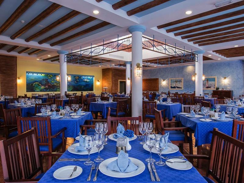 Großer Restaurantraum mit blauen Tischdecken, Holzmöbeln, weißen Säulen und Deckenstrahlern.