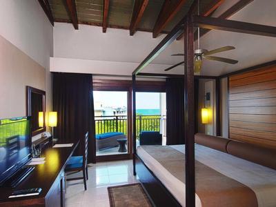 Hotelzimmer mit Doppelbett, Holzmöbeln, TV, Schreibtisch und Balkon mit Meerblick.