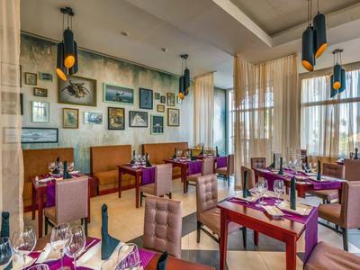 Elegantes Restaurant mit lila Stühlen, Holzrahmen, vielen Bildern und großen Fenstern.