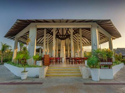 Offener Pavillon mit Holztischen und Stühlen, umgeben von Pflanzen, im Freien bei Sonnenuntergang.