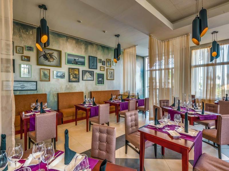 Elegantes Restaurant mit lila Stühlen, Holzrahmen, vielen Bildern und großen Fenstern.