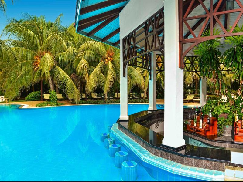 Ein türkisfarbener Pool mit Bar am Rand, grünen Palmen und blauem Himmel im Hintergrund.