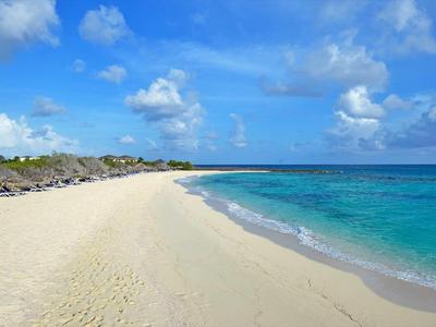 Weißer Sandstrand mit türkisfarbenem Wasser, blauem Himmel und vereinzelt Wolken.