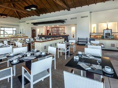 Moderner Speiseraum mit weißen Stühlen, schwarzen Tischen und Holzdach mit Balken.