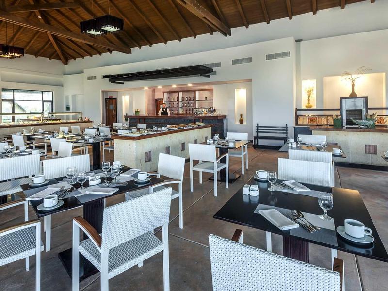 Moderner Speiseraum mit weißen Stühlen, schwarzen Tischen und Holzdach mit Balken.