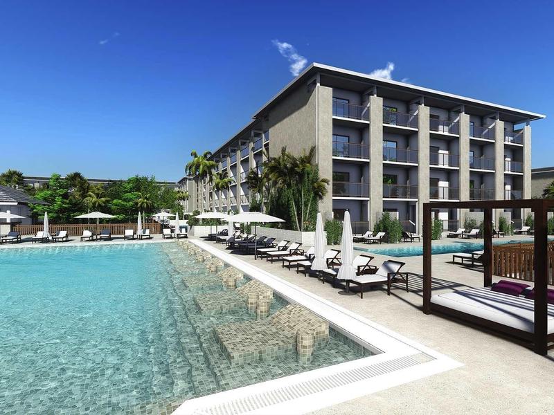 Großes Hotelgebäude mit Pool, Liegestühlen und blauem Himmel in sonniger Umgebung.