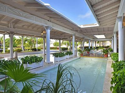 Moderner überdachter Außenpool mit Pflanzen, Säulen und blauem Himmel im Hintergrund.